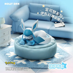 "La boîte surprise Eeveelution endormie présente une figurine Givrali reposant sur un coussin bleu, parfaite pour les collectionneurs de Pokémon."