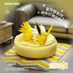 Boîte surprise Eeveelution endormie mettant en vedette un Voltali endormi sur un coussin jaune.