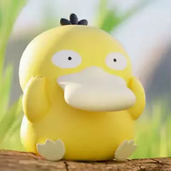 Boîte surprise de mini-figurines Pokémon avec une adorable figurine jaune de Psykokwak sur une surface en bois dans la nature.